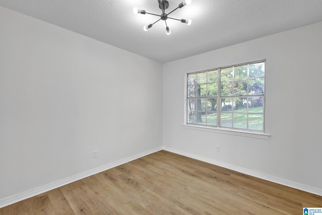 unfurnished room with baseboards, a chandelier, a textured ceiling, and light wood-style flooring