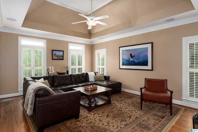 living room featuring wood finished floors, baseboards, a raised ceiling, a ceiling fan, and crown molding