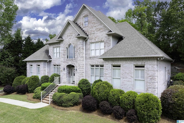 french country style house featuring a front yard, a shingled roof, and brick siding
