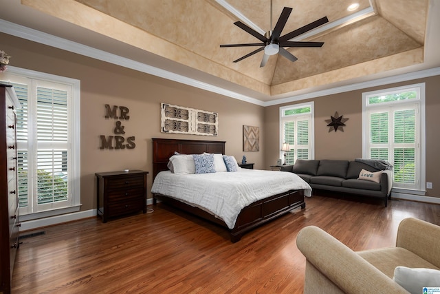 bedroom with wood finished floors, baseboards, visible vents, a raised ceiling, and crown molding