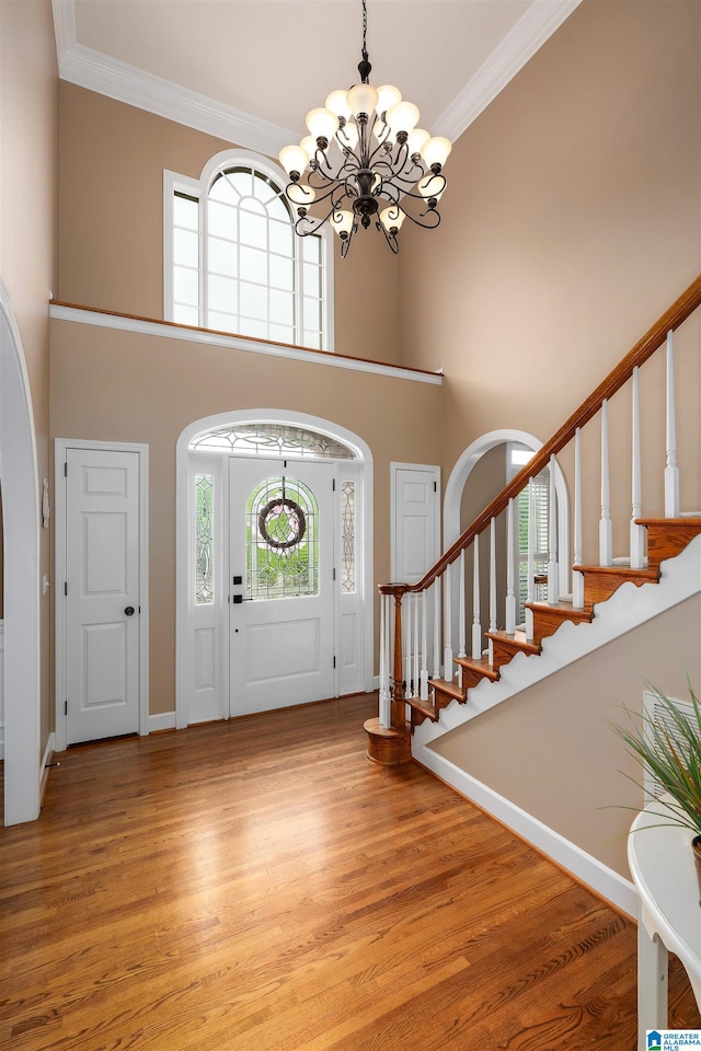 foyer entrance with a high ceiling, a chandelier, stairs, ornamental molding, and arched walkways