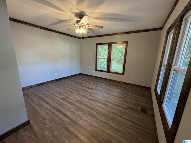 spare room with visible vents, a ceiling fan, ornamental molding, baseboards, and dark wood-style flooring