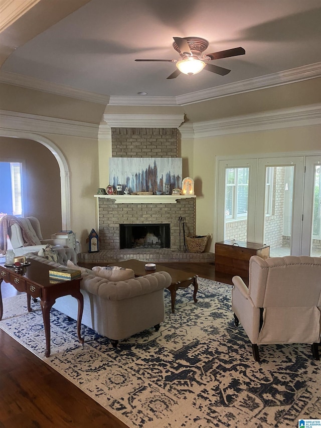 living room with a ceiling fan, crown molding, wood finished floors, arched walkways, and a fireplace