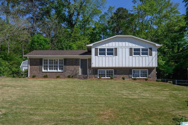 tri-level home featuring board and batten siding, a front lawn, brick siding, and fence