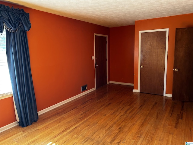 unfurnished room with visible vents, baseboards, wood finished floors, and a textured ceiling