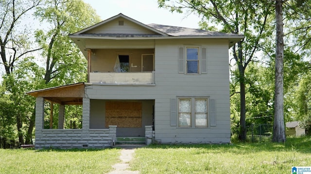 view of front facade with a shingled roof, a balcony, and a front yard