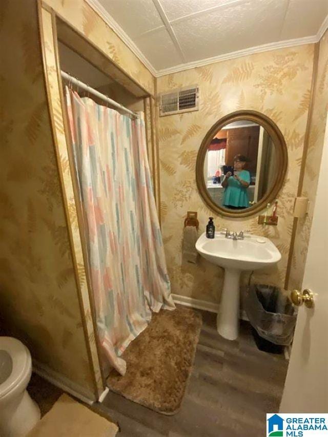 bathroom with ornamental molding, wallpapered walls, wood finished floors, and visible vents