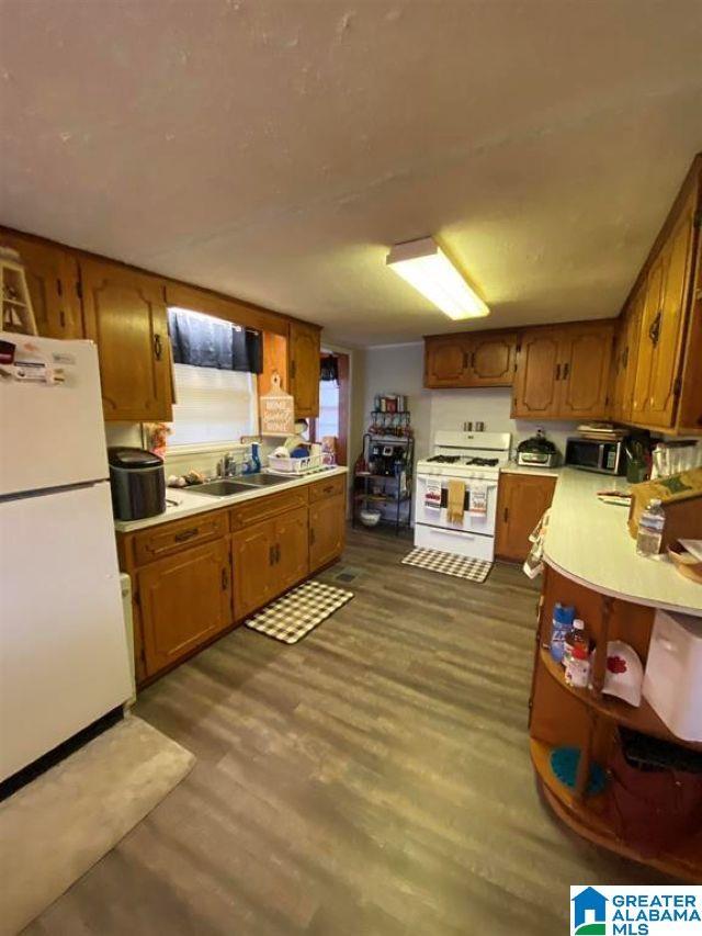 kitchen with a sink, brown cabinets, white appliances, light countertops, and dark wood finished floors