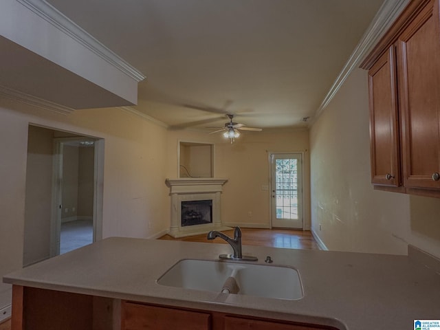kitchen featuring brown cabinets, a fireplace with raised hearth, a ceiling fan, and a sink