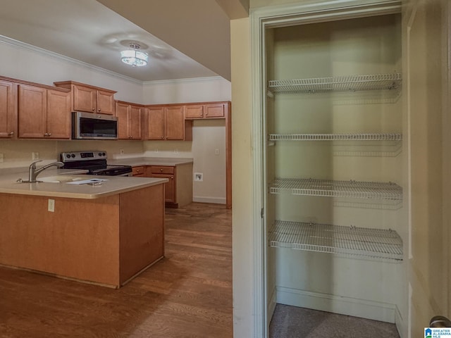 kitchen featuring stainless steel appliances, a sink, wood finished floors, brown cabinetry, and ornamental molding