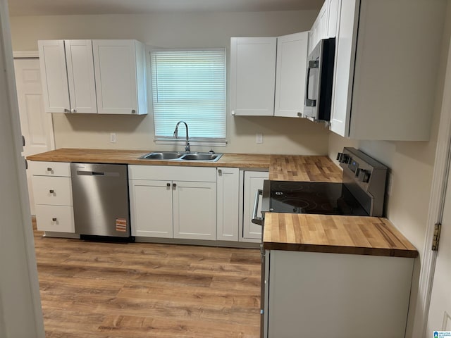 kitchen with a sink, butcher block countertops, light wood-style flooring, appliances with stainless steel finishes, and white cabinetry
