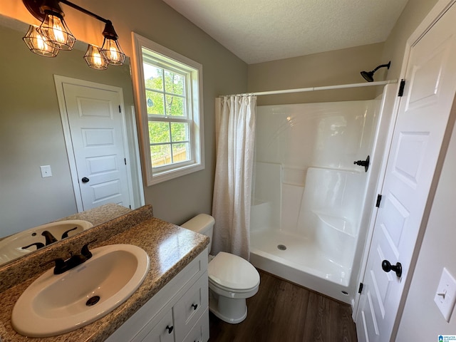 bathroom with a textured ceiling, toilet, a stall shower, wood finished floors, and vanity