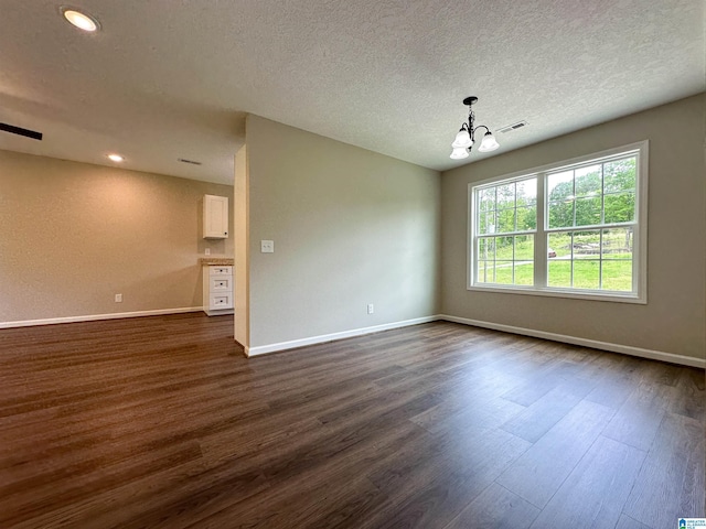 empty room with a textured ceiling, baseboards, visible vents, a notable chandelier, and dark wood-type flooring