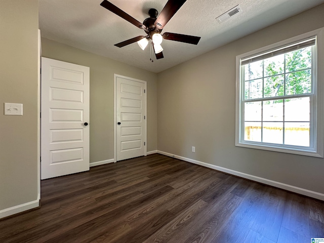 unfurnished bedroom with a closet, ceiling fan, baseboards, dark wood-style flooring, and visible vents