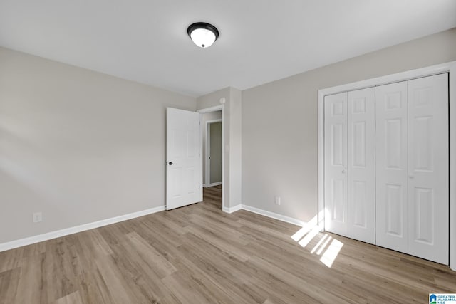 unfurnished bedroom featuring light wood-type flooring, a closet, and baseboards