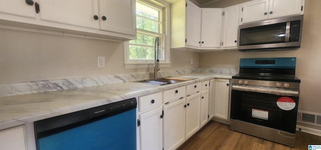 kitchen with stainless steel appliances, a sink, dark wood-type flooring, light stone countertops, and white cabinetry