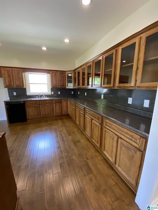 kitchen with dark countertops, a sink, brown cabinetry, dark wood-style flooring, and black dishwasher