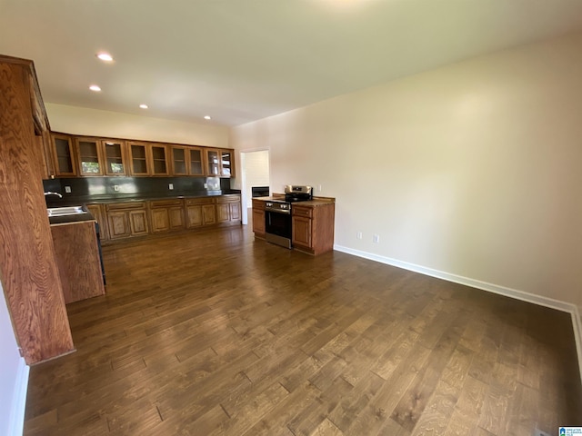 kitchen featuring dark countertops, electric stove, a sink, brown cabinets, and dark wood-type flooring