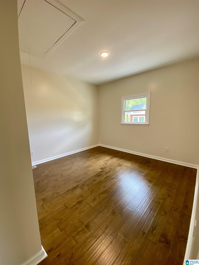 empty room featuring attic access, baseboards, and dark wood-style flooring