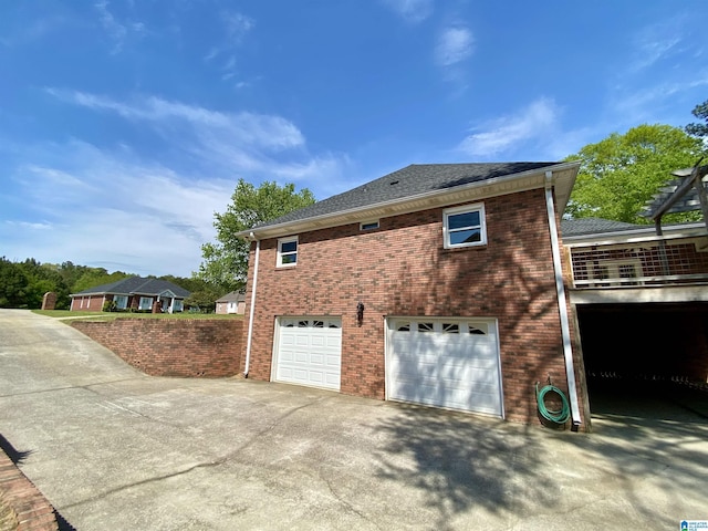 view of side of home featuring an attached garage, brick siding, driveway, and a shingled roof