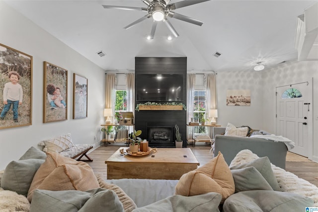 living area with vaulted ceiling, visible vents, light wood-type flooring, a fireplace, and ceiling fan