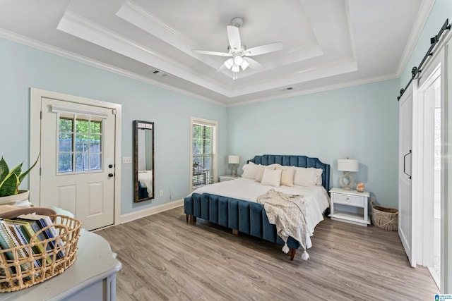 bedroom featuring a barn door, light wood-style floors, a raised ceiling, ornamental molding, and visible vents