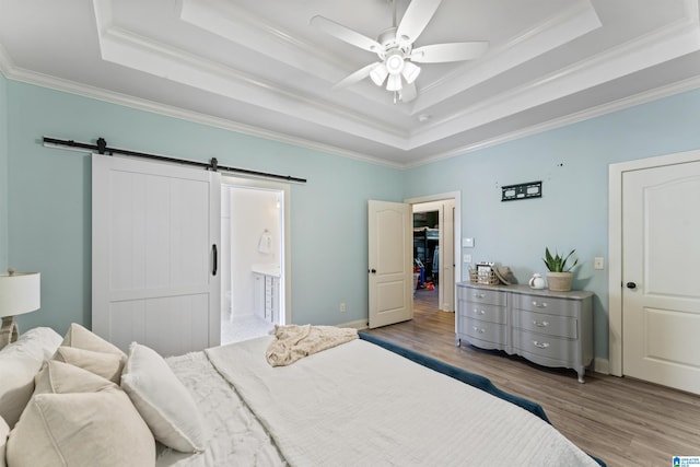 bedroom with crown molding, wood finished floors, a tray ceiling, and a barn door