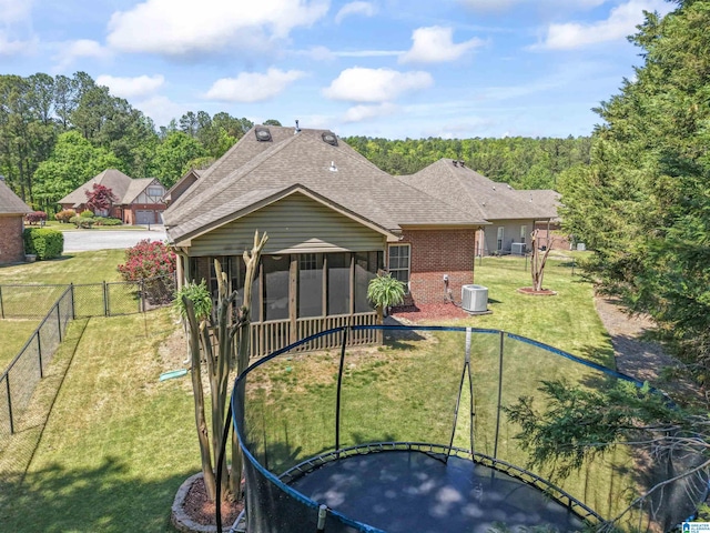 rear view of property with a shingled roof, a yard, brick siding, a sunroom, and a trampoline