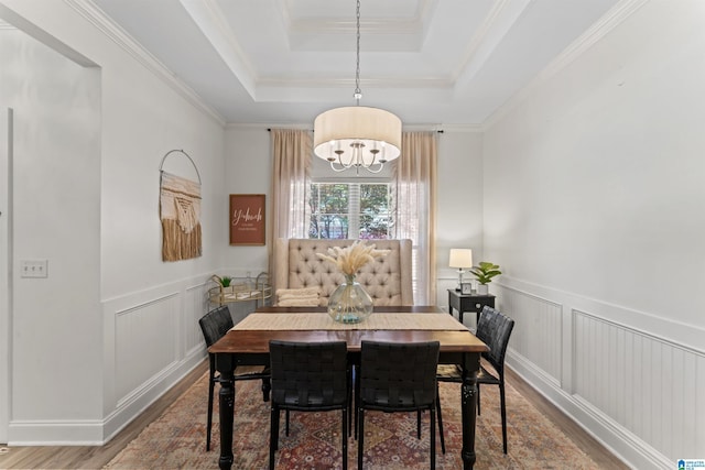 dining area featuring wainscoting, a notable chandelier, wood finished floors, a decorative wall, and a raised ceiling