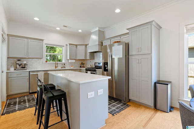 kitchen with a center island, tasteful backsplash, light wood-type flooring, stainless steel appliances, and custom range hood