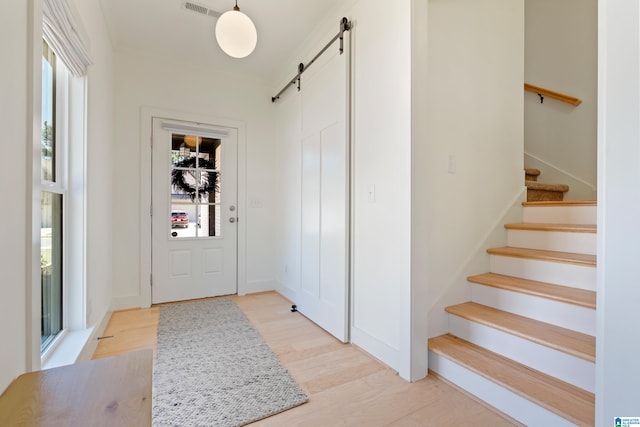 entrance foyer featuring a barn door, stairs, and light wood finished floors