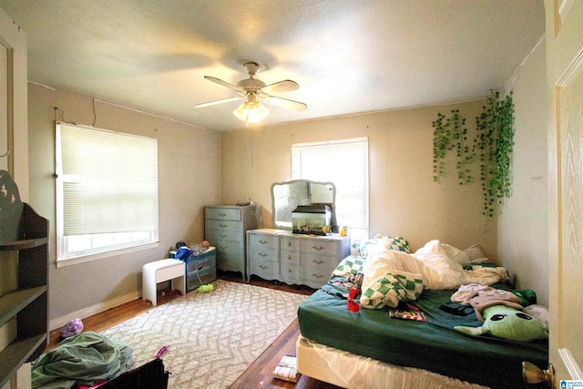 bedroom featuring baseboards, wood finished floors, ceiling fan, and multiple windows