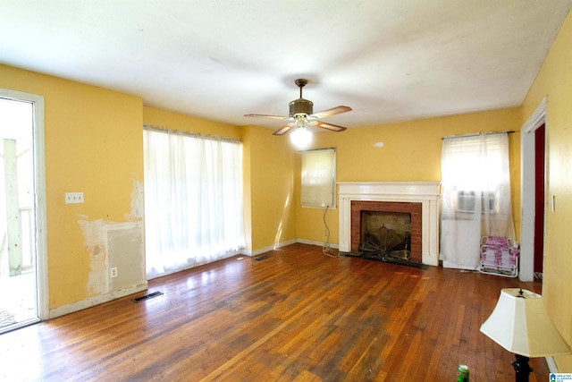 unfurnished living room featuring wood finished floors, a brick fireplace, visible vents, and a healthy amount of sunlight