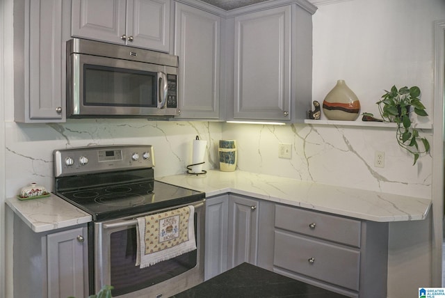 kitchen with decorative backsplash, light stone counters, appliances with stainless steel finishes, and gray cabinets