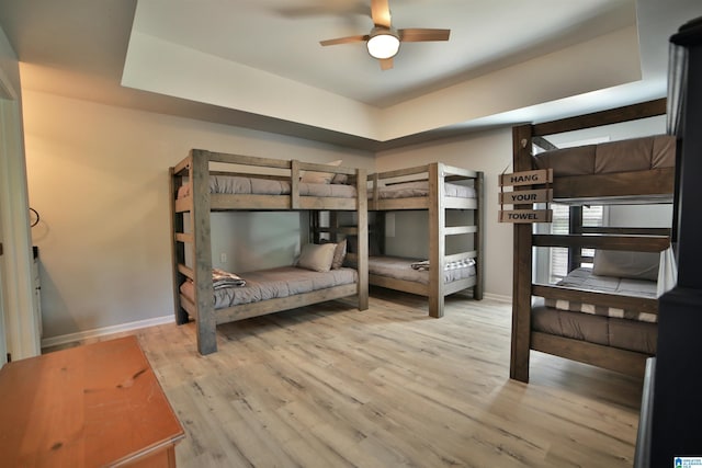 bedroom featuring wood finished floors, a tray ceiling, and baseboards