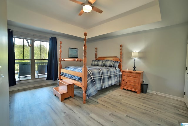 bedroom featuring wood finished floors, a ceiling fan, a tray ceiling, and baseboards