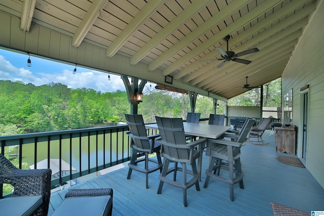 wooden terrace with outdoor dining area, a ceiling fan, and a forest view