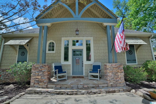 view of exterior entry featuring a shingled roof and covered porch