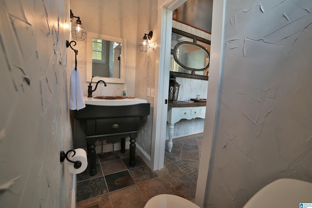 half bath featuring stone tile floors, vanity, and toilet