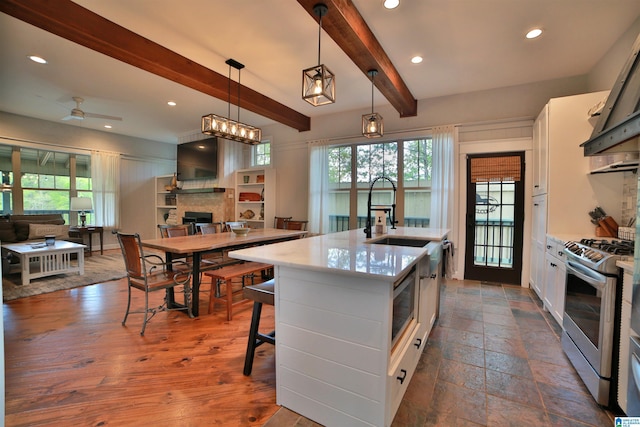 kitchen with beamed ceiling, appliances with stainless steel finishes, a fireplace, white cabinetry, and open floor plan