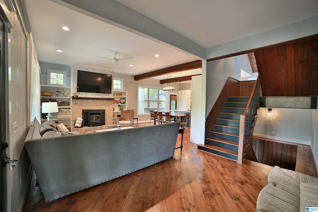 living room featuring wood finished floors, stairs, plenty of natural light, ceiling fan with notable chandelier, and a fireplace