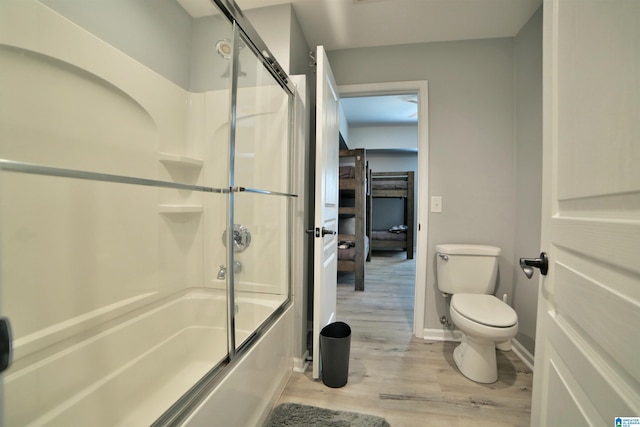 bathroom featuring enclosed tub / shower combo, baseboards, wood finished floors, and toilet