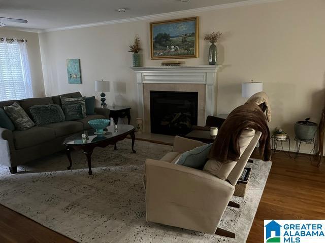 living room featuring wood finished floors, a fireplace with raised hearth, and crown molding