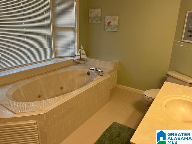 bathroom featuring vanity, a whirlpool tub, baseboards, toilet, and tile patterned flooring