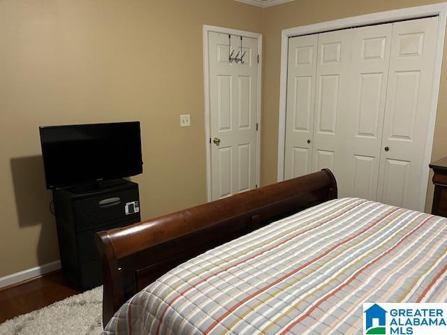 bedroom featuring wood finished floors, a closet, crown molding, and baseboards