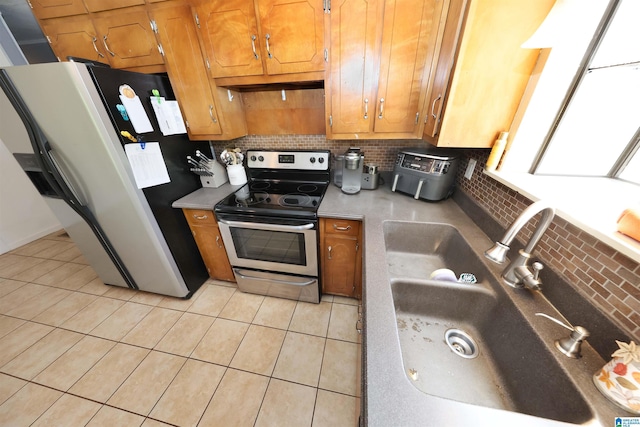 kitchen with a sink, brown cabinetry, decorative backsplash, stainless steel electric range, and freestanding refrigerator