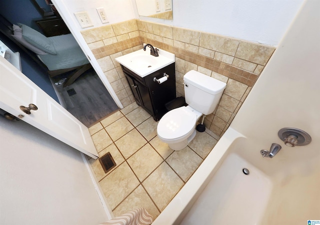 bathroom with tile patterned floors, visible vents, toilet, vanity, and tile walls