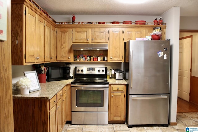 kitchen featuring under cabinet range hood, light stone countertops, a textured ceiling, and appliances with stainless steel finishes