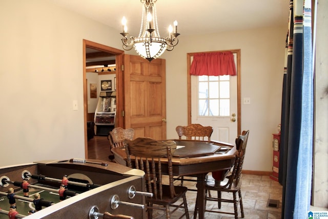 dining room featuring baseboards, visible vents, stone finish flooring, and an inviting chandelier