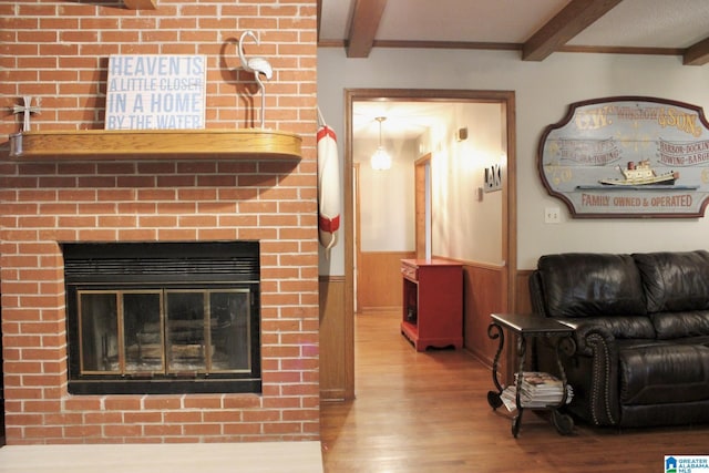 living room featuring a fireplace, wood finished floors, a wainscoted wall, and beamed ceiling